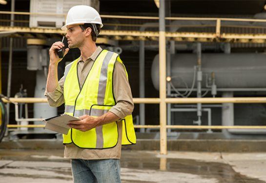 construction worker wearing a yellow safety vest and a white helmet on a walkie talkie
