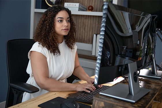 An African American woman wearing a white shirt is sitting in an office working on a computer.