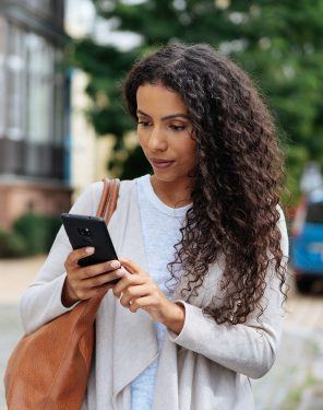 Young woman looking at her mobile phone as she reads a text message outdoors in a town street