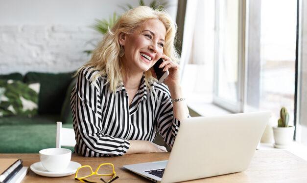 Woman smiling while taking a call and working from home on her laptop.